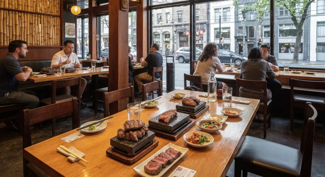 Kingyo Izakaya en Denman Street, un comedor de madera cálida y bambú con carne a la piedra y platos pequeños sobre la mesa